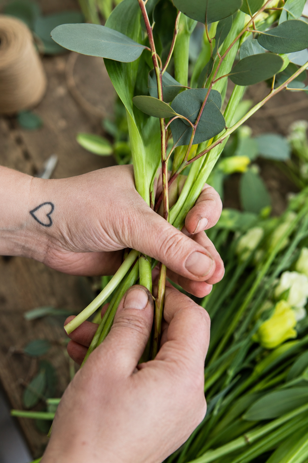 Hände führen grüne Blumenstiele und Eukalyptus beim Binden eines Straußes zusammen
